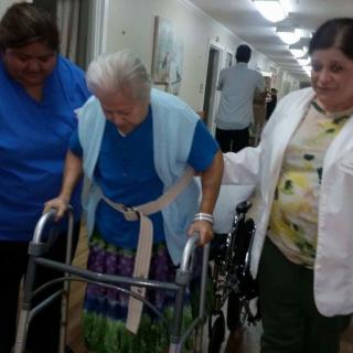 An elderly person receiving assistance from caregivers while using a walker in a nursing home.