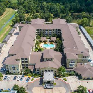 Aerial view of a residential complex with a central swimming pool, surrounded by greenery and parking areas.