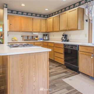 A modern kitchen with wooden cabinets and ample countertop space, featuring various appliances under natural lighting.