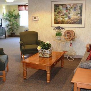 A cozy living room with comfortable chairs, a wooden coffee table, decorative plants, and a framed picture on the wall.
