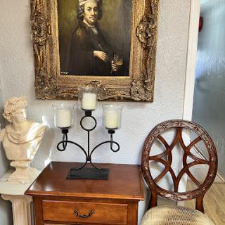 A vintage corner featuring a portrait, elegant chair, and decorative bust.