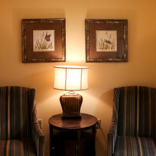 A cozy corner of a living room featuring two striped chairs, a lamp on a side table, and framed artwork on the wall.