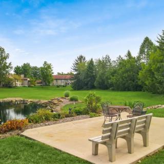 A peaceful patio overlooking a pond surrounded by lush greenery and trees.