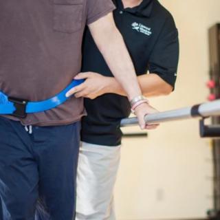 A physical therapist assists a person with walking exercises using a supportive belt.