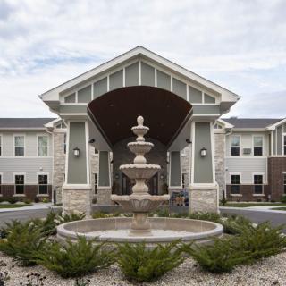 A symmetrical building entrance with a central fountain and landscaped surroundings.