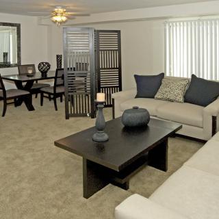A well-decorated living room with neutral tones featuring a sofa, coffee table, and dining area.
