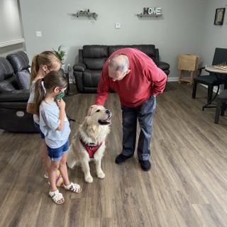An elderly man and two children pet a dog in a living room.