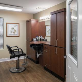 A modern hair salon interior with a styling chair, mirror, and wooden cabinets.