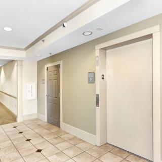 A well-lit hallway with an elevator and a side door, featuring tiled flooring.