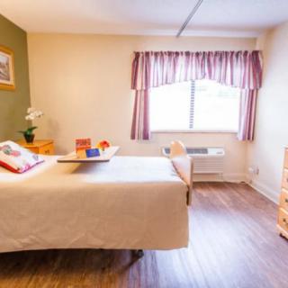 A cozy bedroom with a neatly made bed, wooden furniture, and natural light streaming through the window.