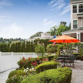 A beautiful garden patio with colorful flowers and an orange umbrella, providing a cozy outdoor seating area next to a house.