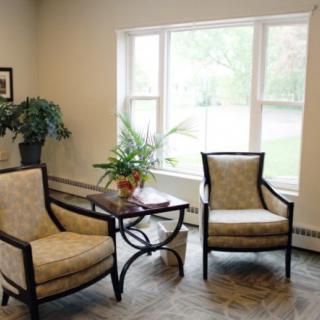 A cozy living room with two chairs, a small table, and plants by the window.