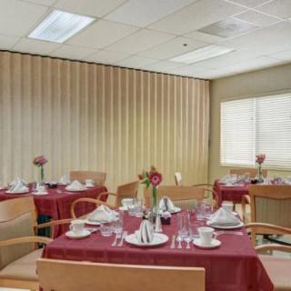 A neatly arranged dining area with tables set for a meal, featuring red tablecloths and floral centerpieces.