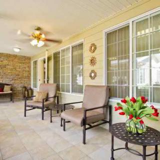 A bright and inviting patio area with comfortable chairs, a table adorned with tulips, large windows, and a ceiling fan.
