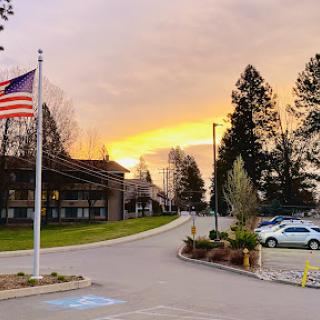 A serene sunset scene with an American flag waving in the foreground, surrounded by trees and buildings.