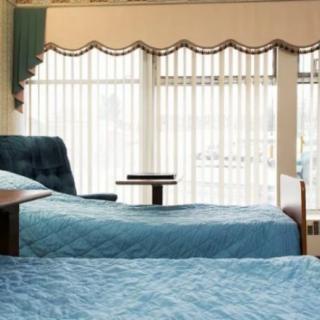 A bright bedroom featuring two neatly made beds with blue bedding and large windows letting in natural light.