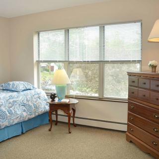 A cozy bedroom with a bed, dresser, and a window letting in natural light.