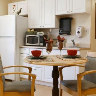 A cozy kitchen and dining area featuring a small round table set for two, with white cabinets and essential appliances.