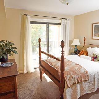 A cozy bedroom with a wooden bed frame and natural light streaming through a large window.