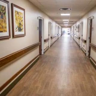 A hospital corridor featuring wooden flooring and framed paintings on the walls.