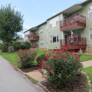 A well-maintained apartment building with balconies, surrounded by landscaped gardens and flowering shrubs.