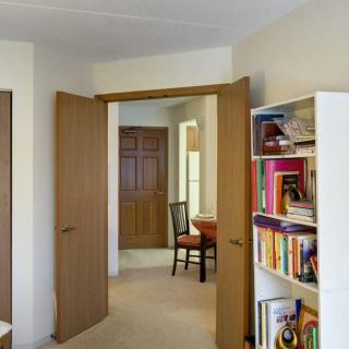 A cozy interior featuring an open doorway, a bookshelf filled with books, and a glimpse of the adjacent room with furniture.