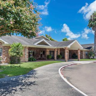 A single-story brick house with a driveway and lush greenery under a clear blue sky.