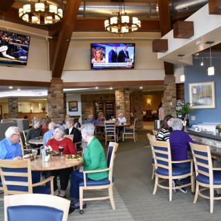 A group of seniors enjoying a meal in a cozy dining area with televisions mounted on the walls.