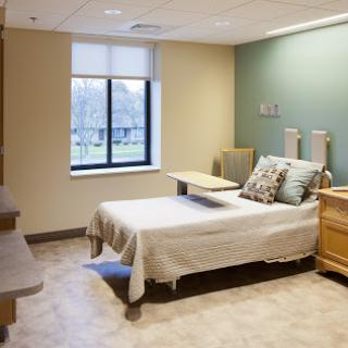 A well-lit hospital room featuring a bed with a clean white cover and a wooden bedside table.
