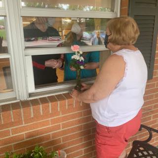 A person handing a flower through a window, engaging with others inside.