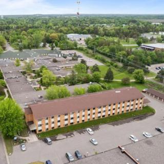 Aerial view of a suburban area featuring a rectangular building with a parking lot surrounded by greenery and roads.
