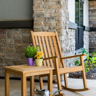 A wooden rocking chair and side table with potted plants on a porch.