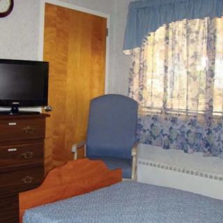A cozy bedroom with a TV, dresser, chair, and window with floral curtains.