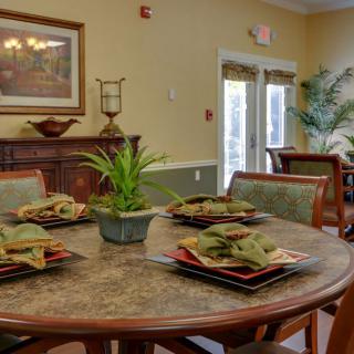 A cozy dining room with a round table set for four, featuring elegant dishware and a decorative plant centerpiece.