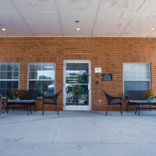 The entrance to a brick building with outdoor seating and glass doors.
