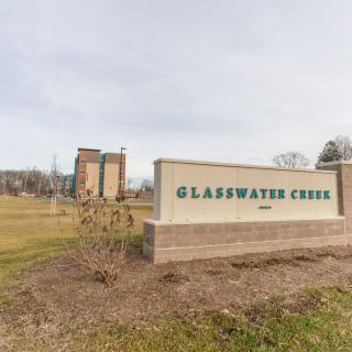Entrance sign for Glasswater Creek with a building and landscaped area in the background.