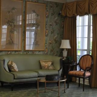 A cozy living room with elegant decor, featuring a green sofa, armchair, and a floor lamp near large windows.