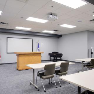 An empty conference room with a podium, projector screen, and rows of tables and chairs.