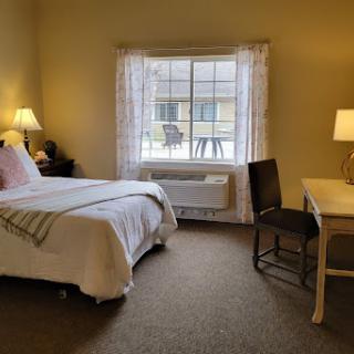 A cozy and well-lit bedroom featuring a bed, desk, and large window.