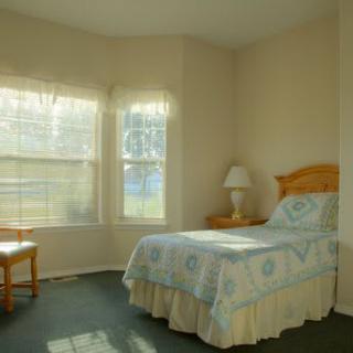 A cozy bedroom featuring a single bed, a lamp, and large windows letting in natural light.