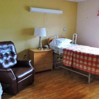 A nursing home room with a hospital bed, chair, and bedside table.