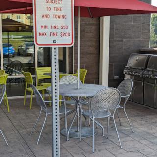 A cozy outdoor dining area featuring a round table with chairs under a red umbrella, accompanied by a grill in the background.