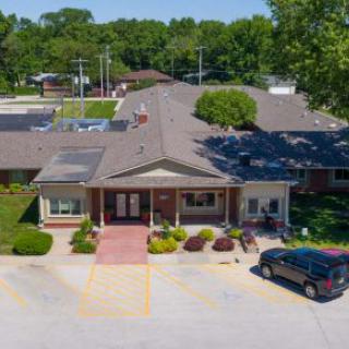Aerial view of a building with a parking lot and cars surrounded by trees on a sunny day.