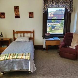 A cozy bedroom with a single bed, nightstand, and a comfortable chair by the window.