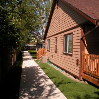 A pathway beside a house with a wooden fence and green lawn under the sunlight.