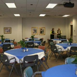 A banquet hall set up for an event with tables covered in blue tablecloths, chairs, and decorations.