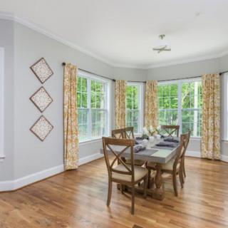 A bright dining room with large windows, hardwood floors, and a wooden table set.