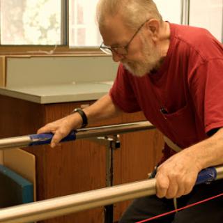 An elderly man using a parallel bar for physical therapy.