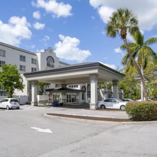 A hotel entrance with a covered driveway and surrounding palm trees under a partly cloudy sky.