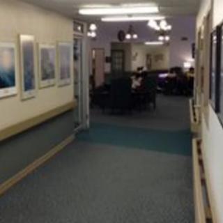 A carpeted hallway with framed artwork on the walls, leading to a seating area.